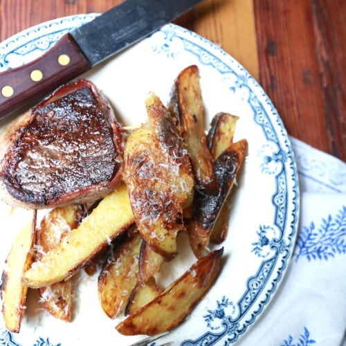 closeup of potato wedge fries on decorative plate with steak