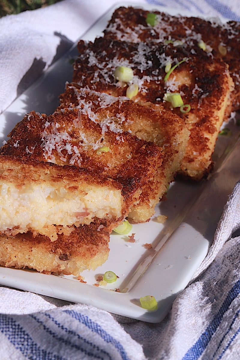 White long plate with fried grits cakes lined up with parmesan cheese and scallions sprinkled on top.