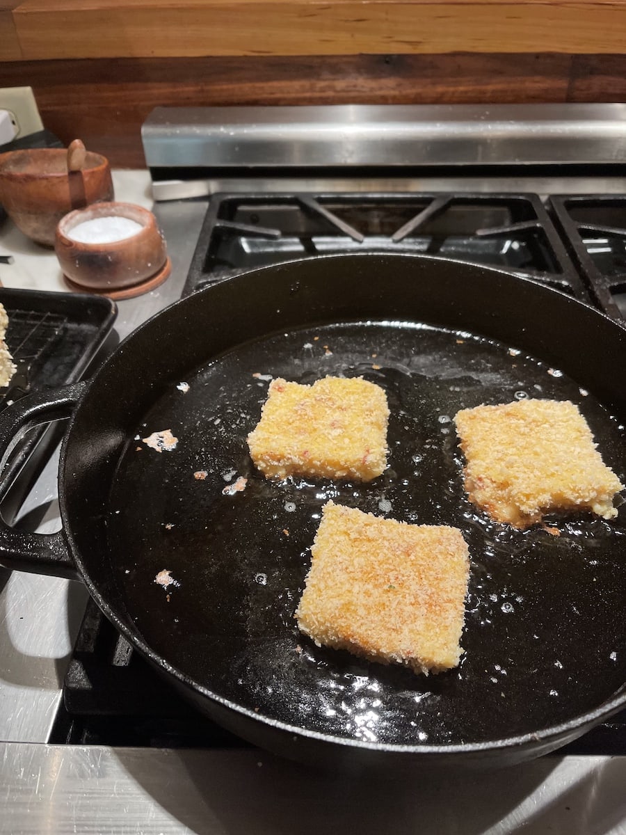 Square grits cakes with Panko in a large skillet with frying oil