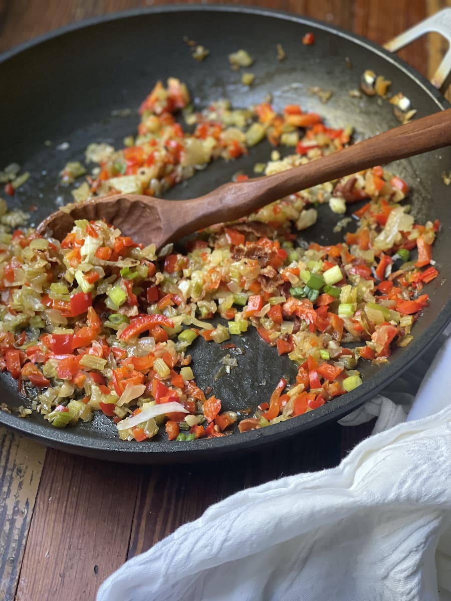 Red Bell Pepper, onions, celery, and garlic diced in a nonstick skillet with a wooden spoon
