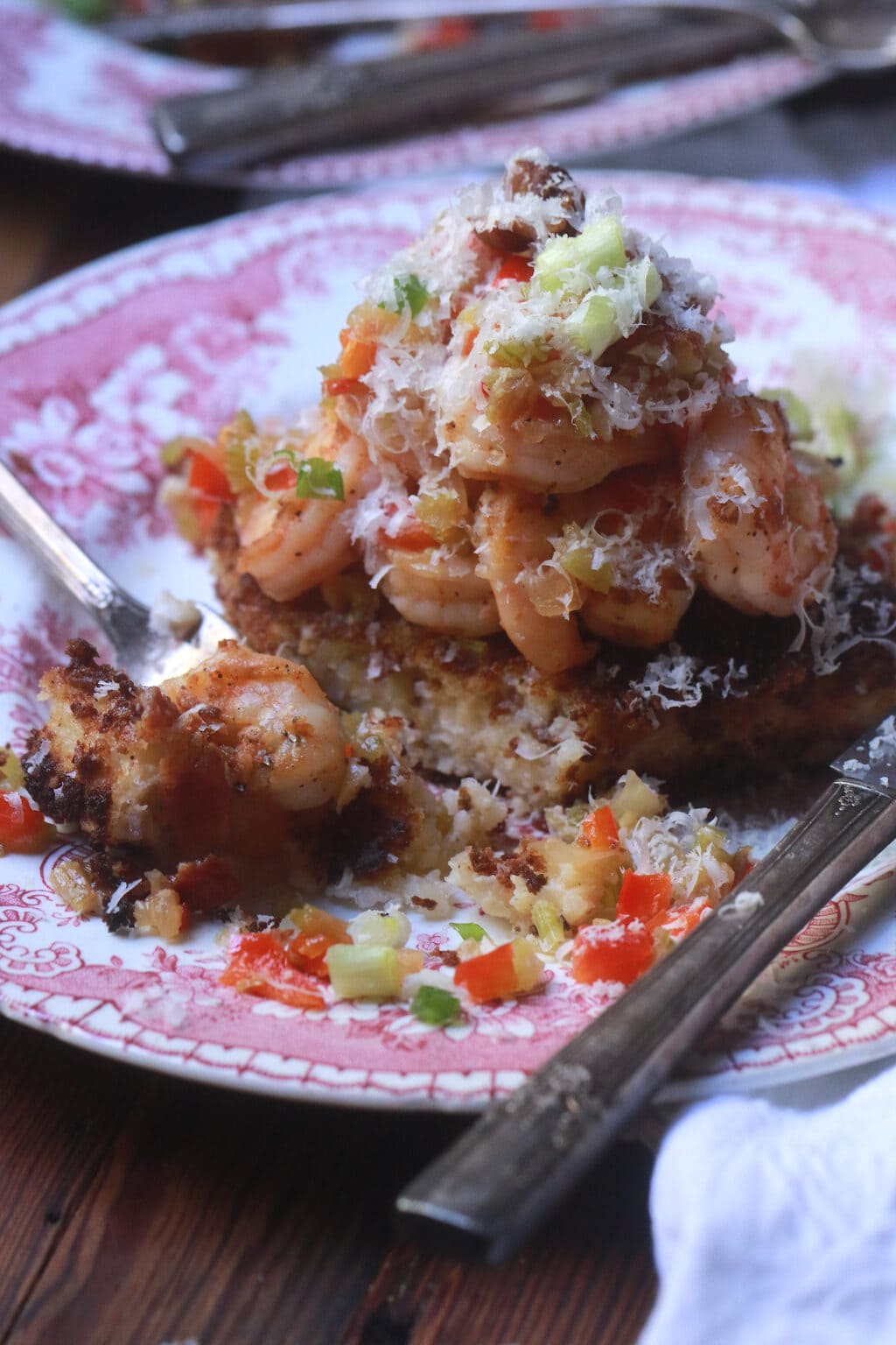 Close up of the pink toile plate with grit cake and shrimp with tons of parmesan cheese piled on top of the shrimp.