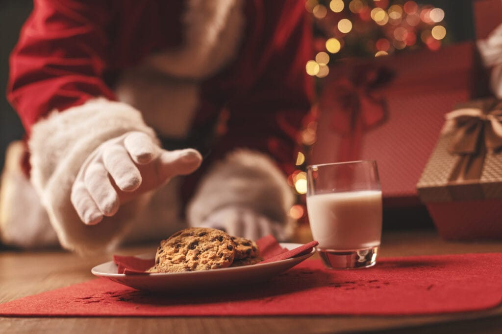 A plate of cookies for Santa with Santa's arm in red costume and white gloves, reaching for cookies