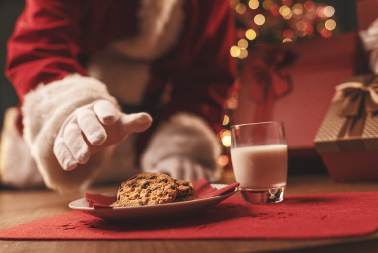 A plate of cookies for Santa with Santa's arm in red costume and white gloves, reaching for cookies