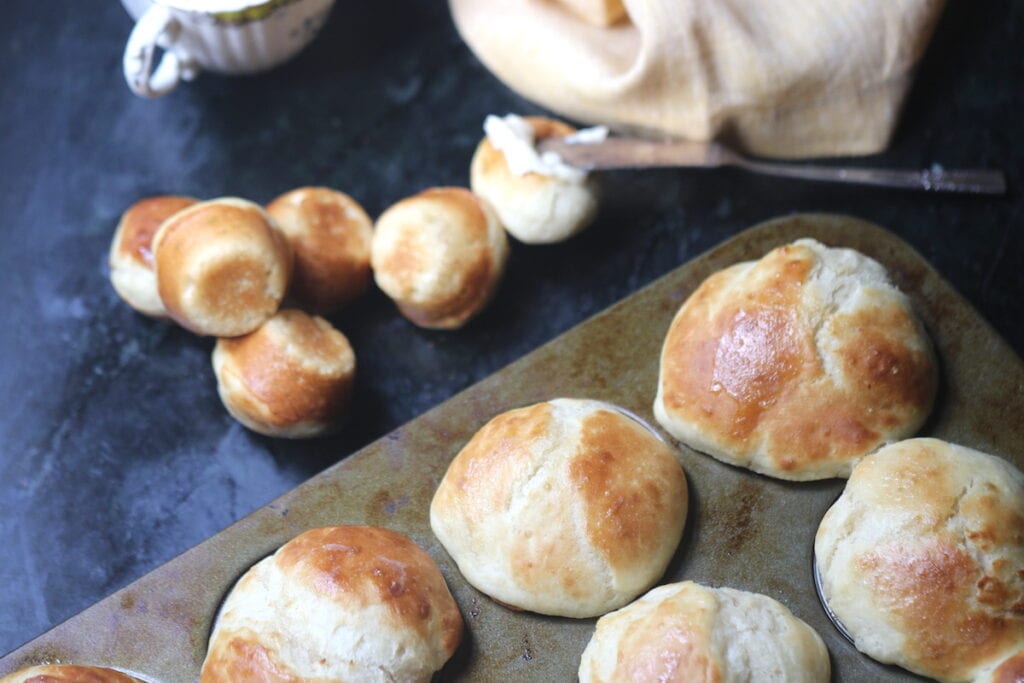 horizontal photo of yeast rolls in a muffin pan and some on the black marble table.