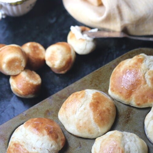 horizontal photo of yeast rolls in a muffin pan and some on the black marble table.