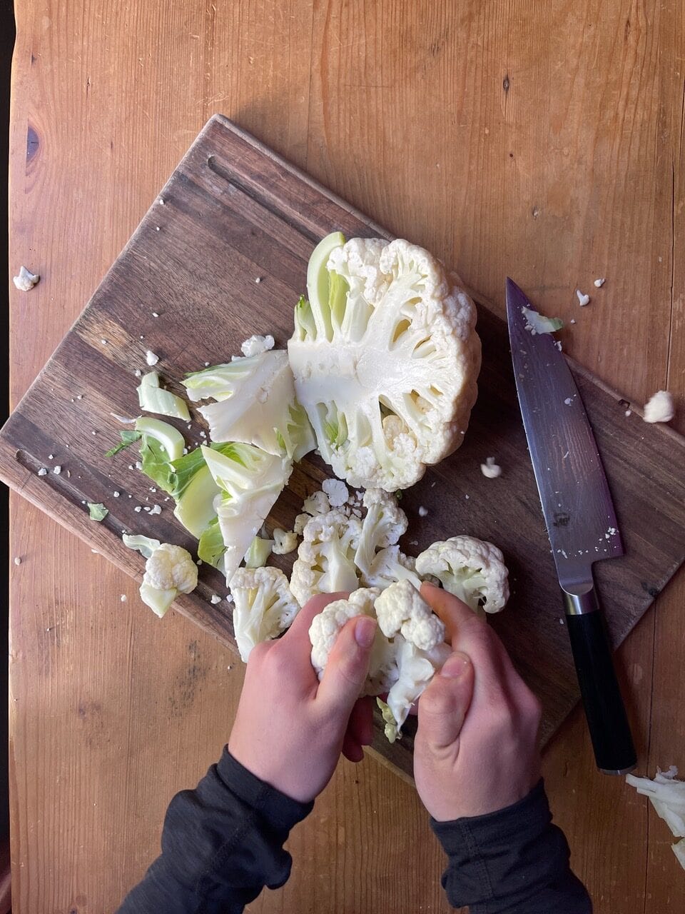 cutting and breaking up cauliflower on wooden board
