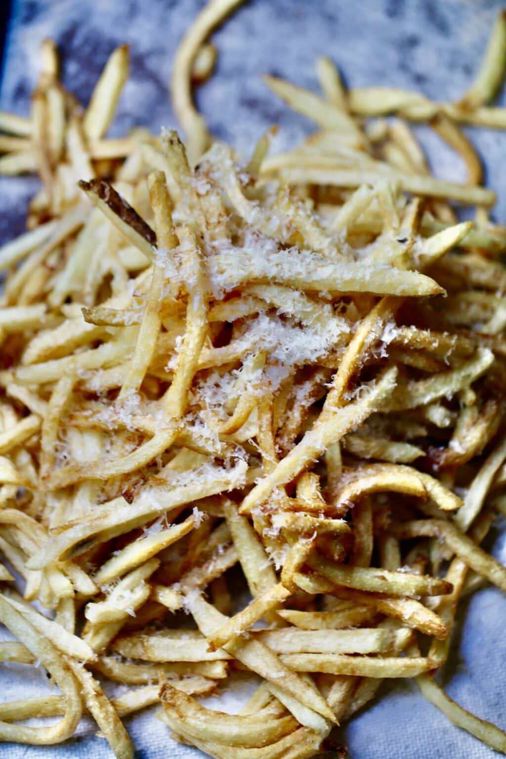 Cooked homemade fries on white kitchen cloth with liberal grating of Parmesan cheese