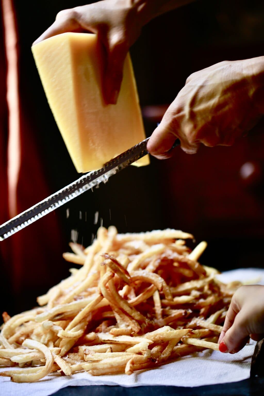 Stacy Lyn grating cheese over homemade French fries - hand reaching to take a fry