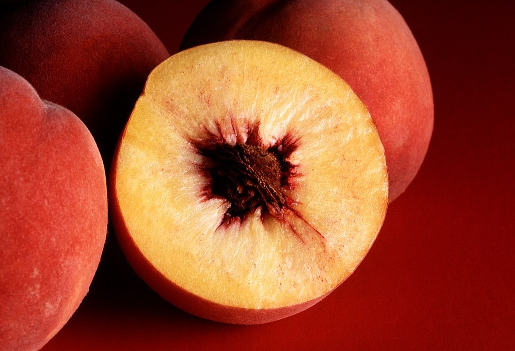fresh peaches, one cut in half to reveal pit