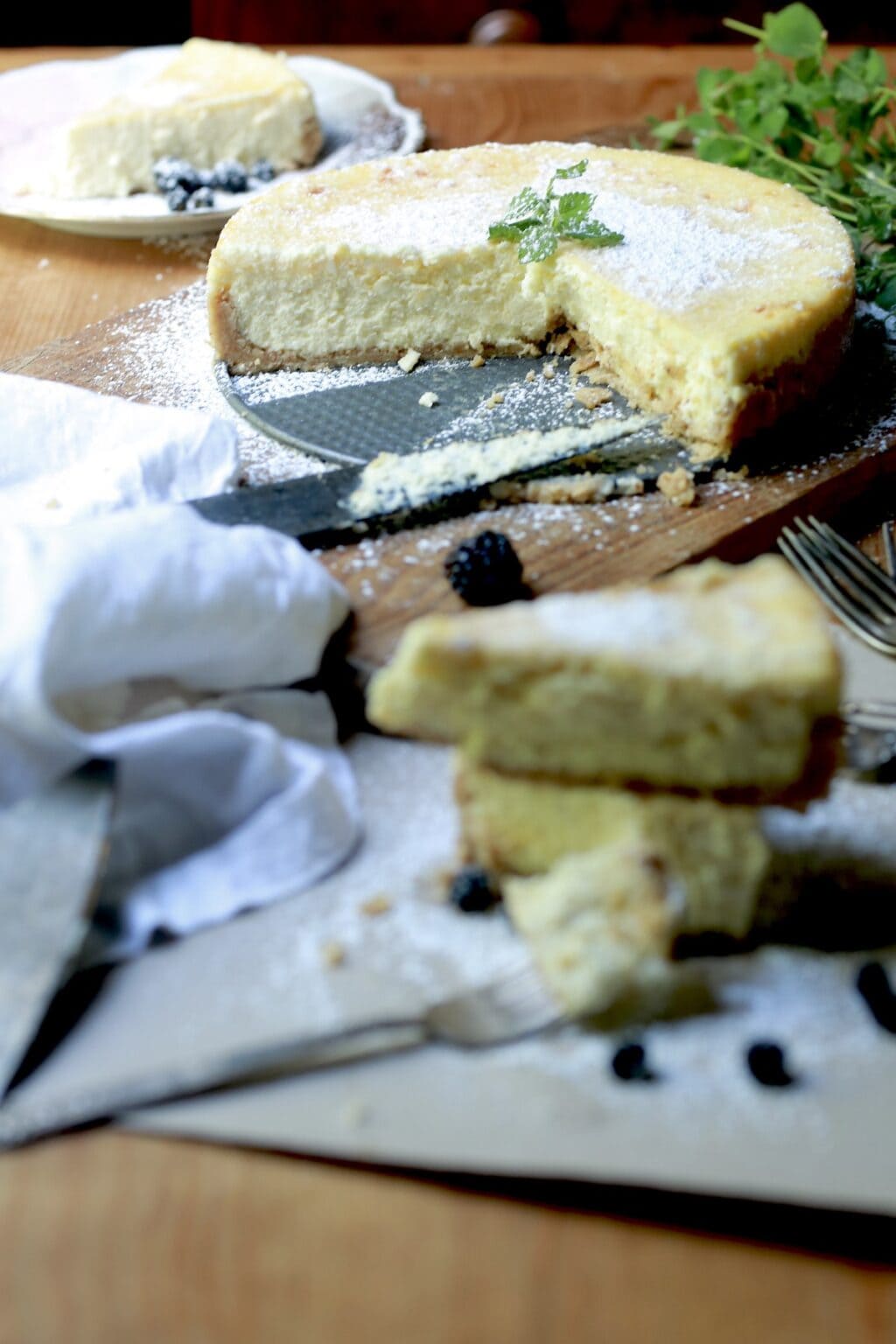 Freshly made Italian cheesecake on pie pan with slices cut out and stacked in front of cake. Slice on decorative plate in background.