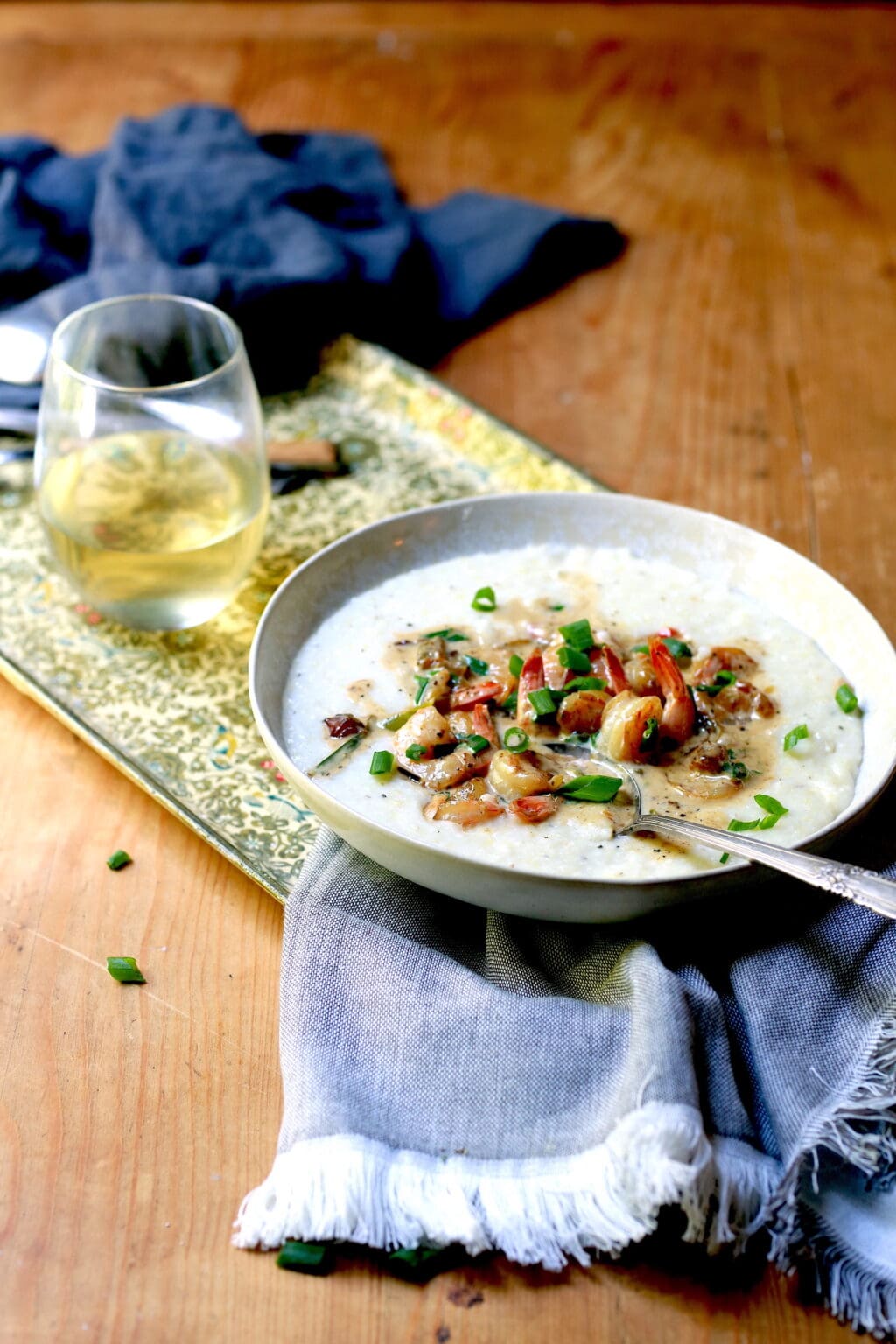 Shrimp and grits in white bowl with spoon, beverage, and napkin