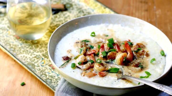 Shrimp and grits in white bowl with spoon, beverage, and napkin