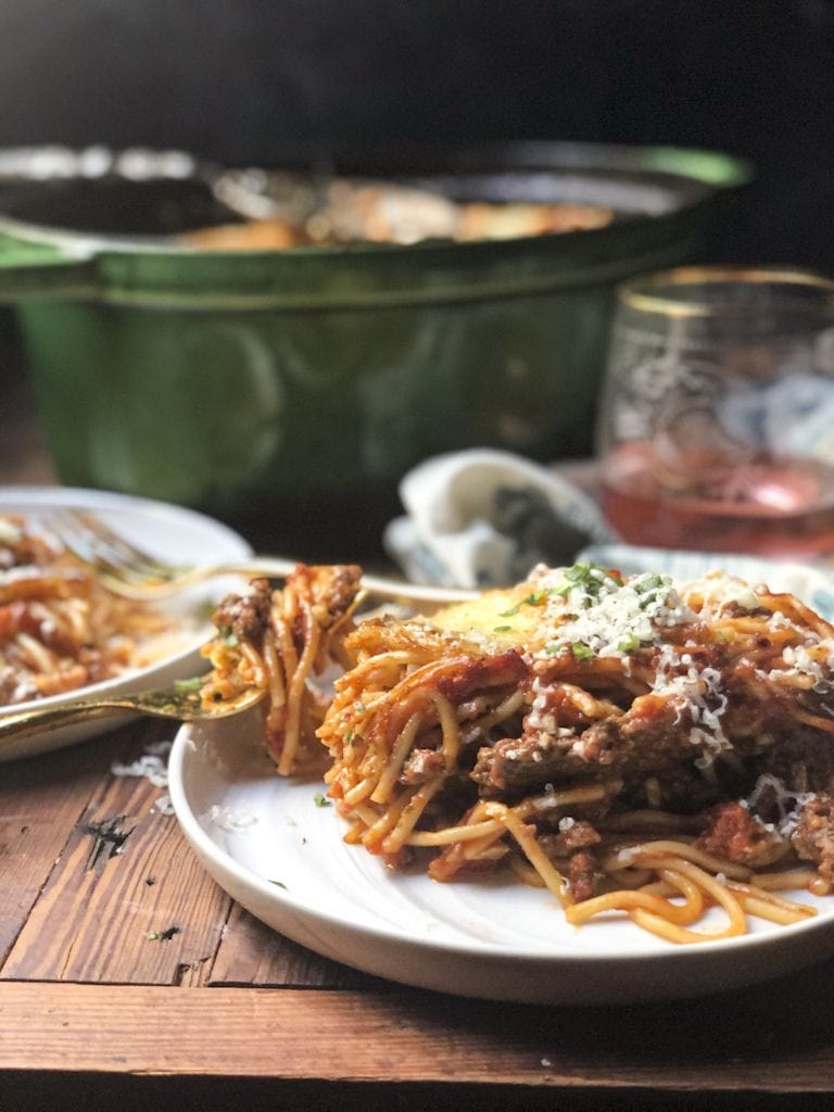 serving of baked cream cheese spaghetti on a white plate with fork with green pot in background