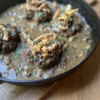 crispy fried onions over hamburger steak in mushroom gravy in cast iron skillet