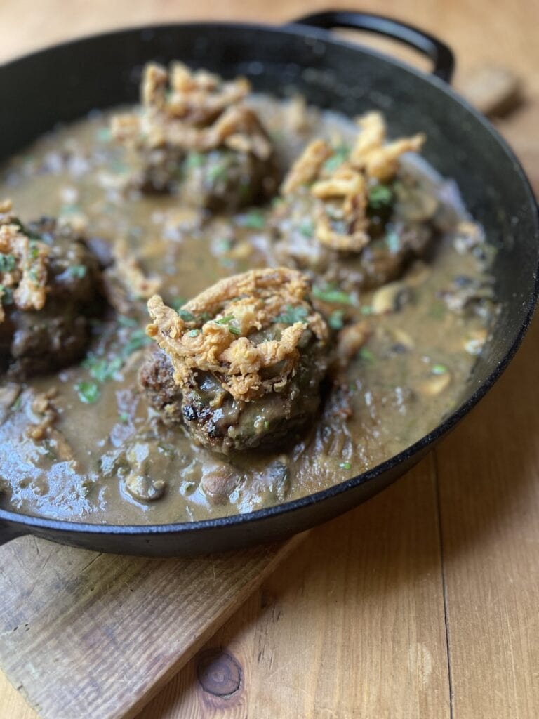 crispy fried onions over hamburger steak in mushroom gravy in cast iron skillet