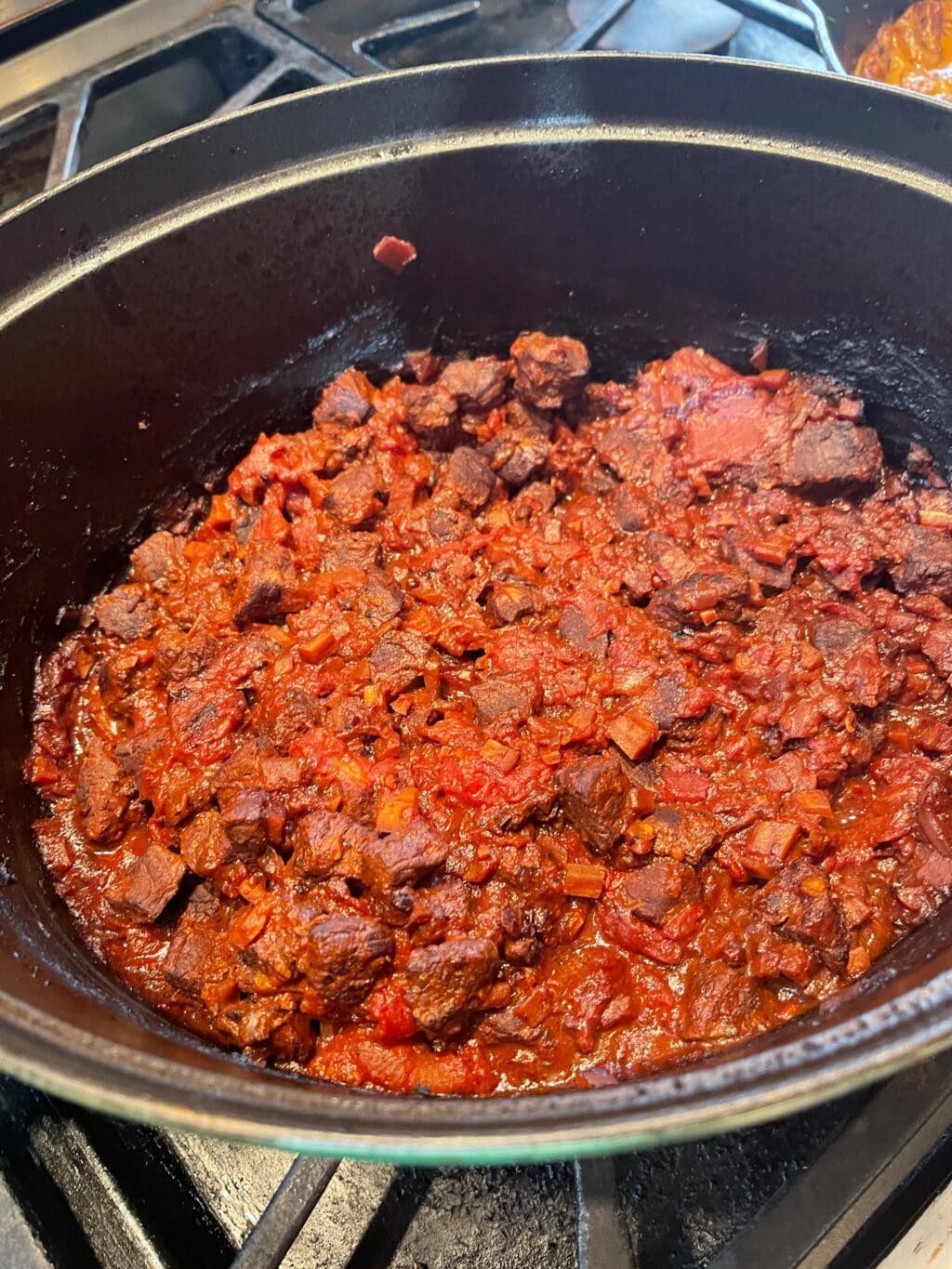 braising meat in Dutch oven on stovetop with tomatoes, vegetables, and red wine