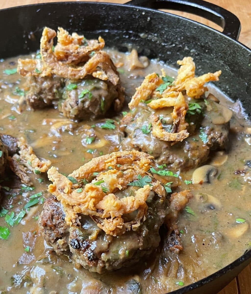 crispy fried onions on hamburger steak in black skillet
