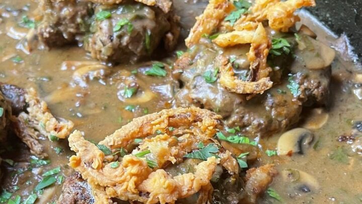 crispy fried onions on hamburger steak in black skillet