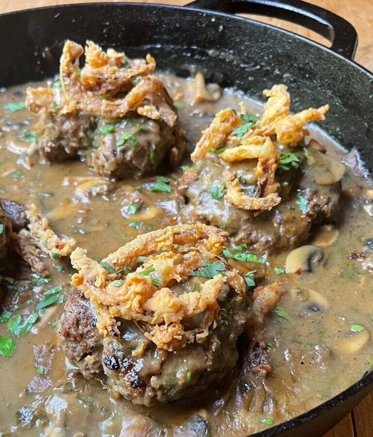 crispy fried onions on hamburger steak in black skillet