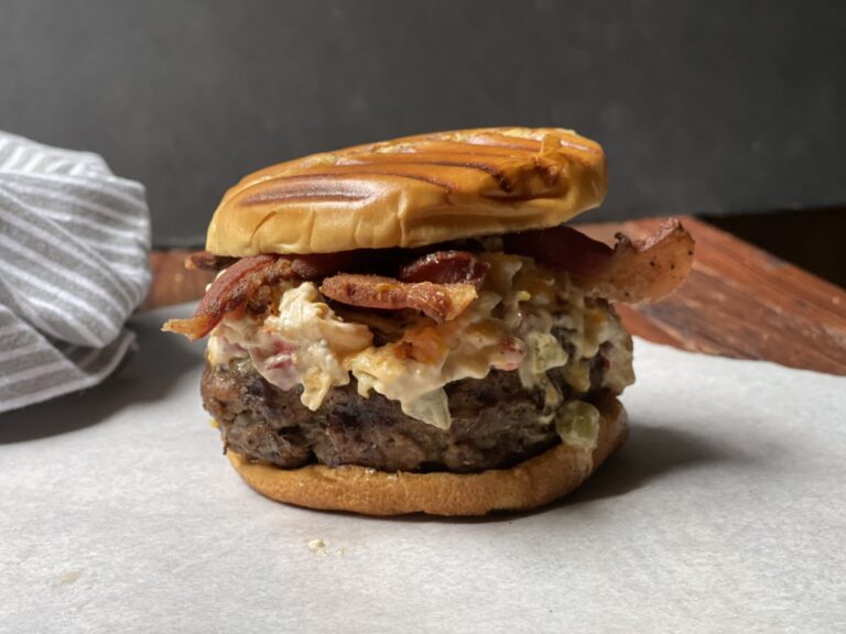 venison burger loaded with bacon and piminento cheese on cutting board