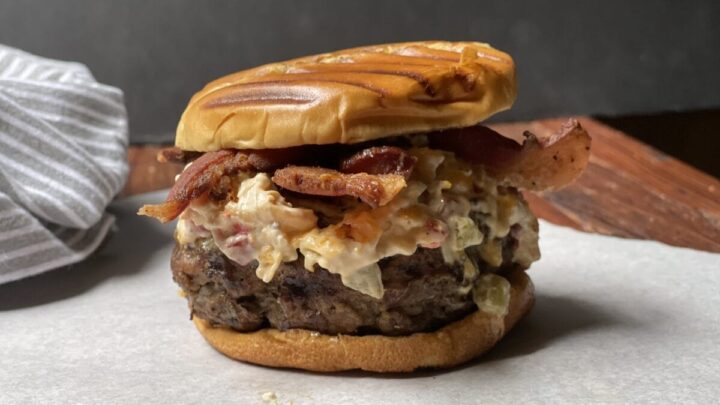 venison burger loaded with bacon and piminento cheese on cutting board