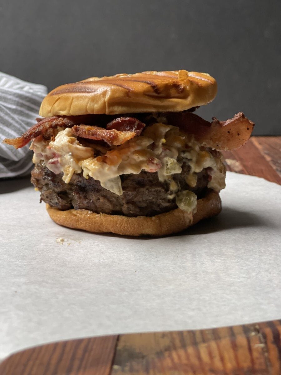 stacked venison bacon pimiento burger with bun on white cutting board