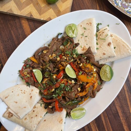 venison fajitas disassembled on white platter with folded tortillas