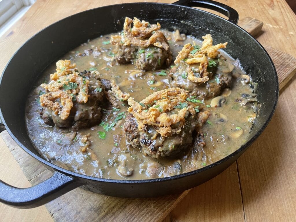 horizontal photo of venison hambuger steak in black skillet with mushrom gravy
