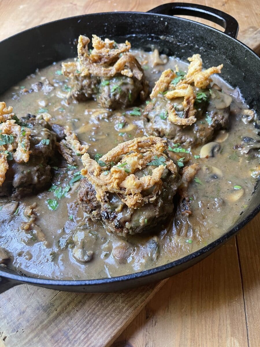 venison hamburger steak with mushroom gravy and crispy fried onions  in black skillet