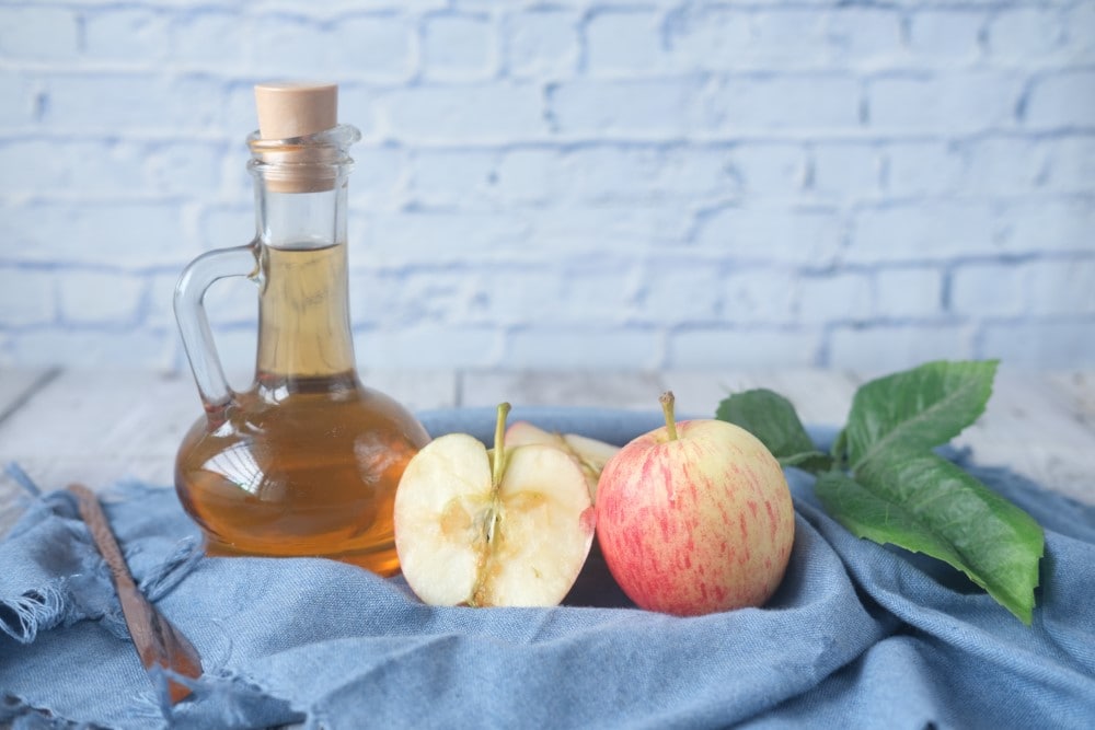 homemade apple cider vinegar in bottle with stopper next to apples on blue cloth