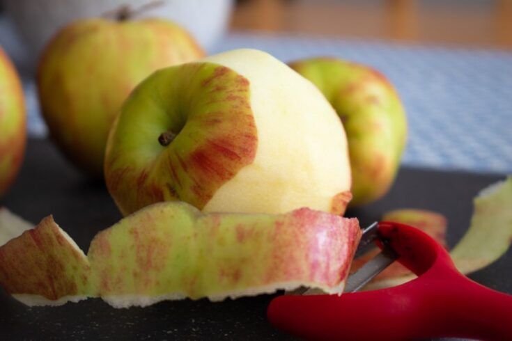 apples with one partially peeled in foreground, red apple peeler