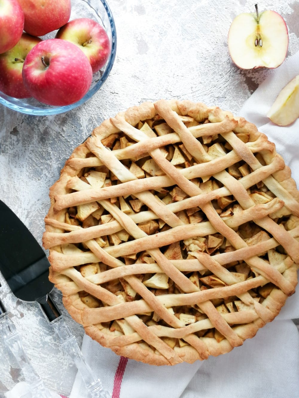 baked apple pie with lattice top crust, bowl of red apples, and sliced apple in background on table