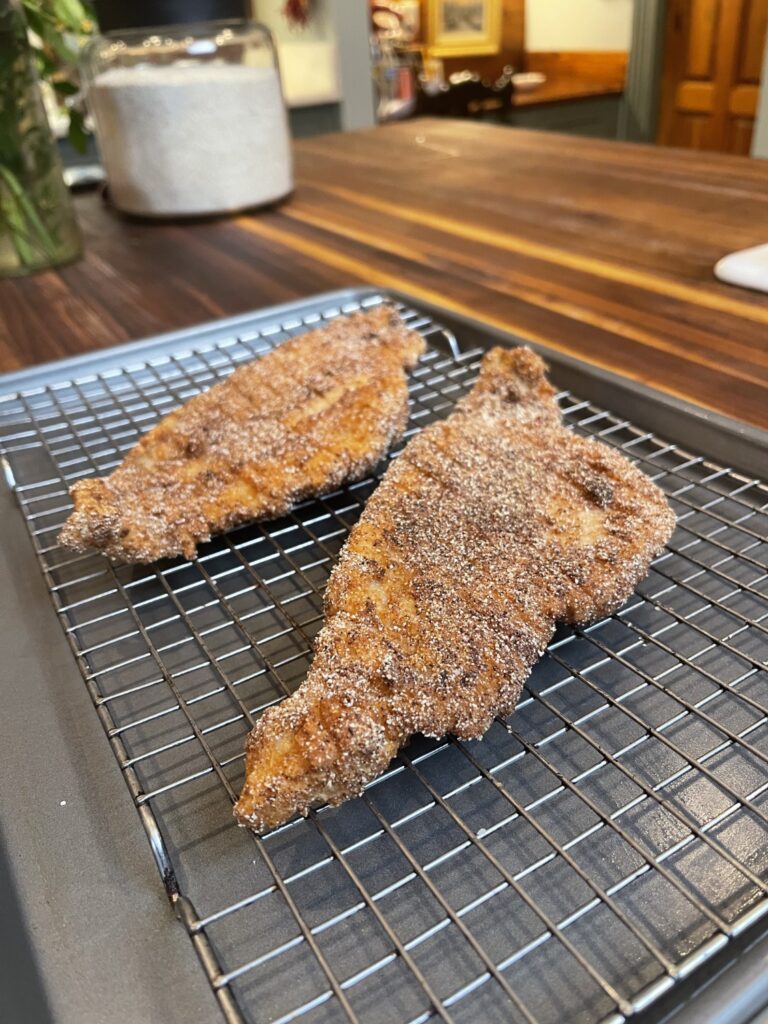 fried catfish cooling on a wire rack over cookie sheet on wooden kitchen counter