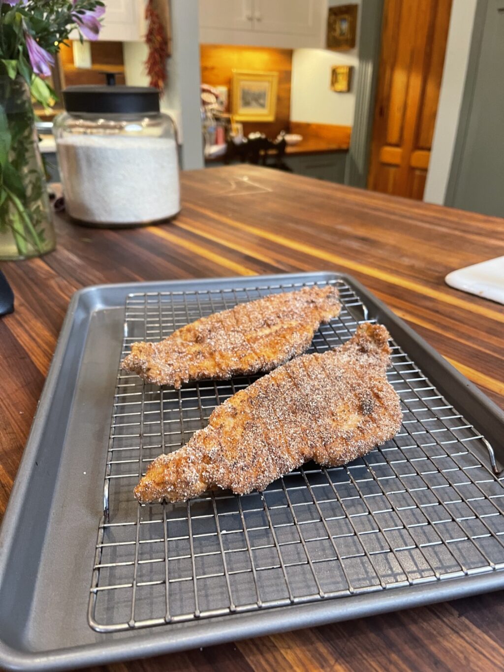 fried catfish on cooking rack over baking sheet in foreground, kitchen in background