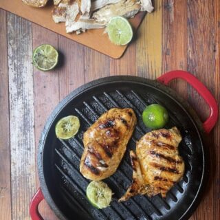 cilantro lime marinated chicken on black grill pan with lime slices; in background is cutting board with sliced chicken breast