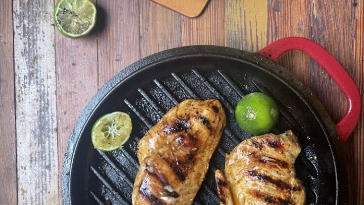 cilantro lime marinated chicken on black grill pan with lime slices; in background is cutting board with sliced chicken breast