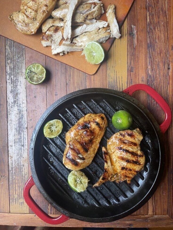 cilantro lime marinated chicken on black grill pan with lime slices; in background is cutting board with sliced chicken breast