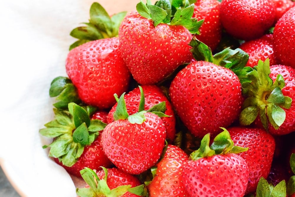 fresh whole strawberries in a white bowl, waiting to be sliced for power salad