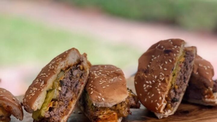 Smash burgers on bun, cut in half and arranged on cutting board behind a bowl of pickle slices