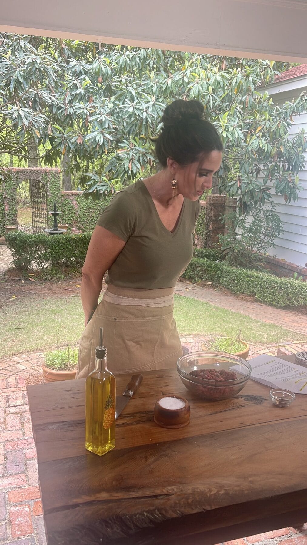 Stacy Lyn outdoors in t-shirt and chef's apron, reading smash burgers recipe with bowl of ground beef mixture on table
