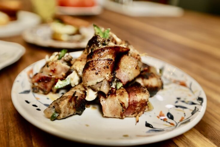 bacon wrapped dove with figs on white, floral pattern plates on wooden kitchen counter