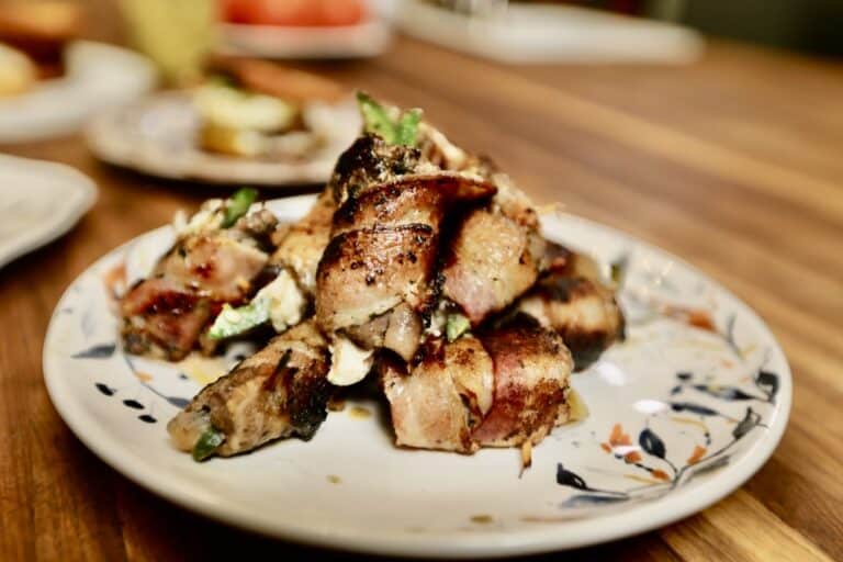 bacon wrapped dove with figs on white, floral pattern plates on wooden kitchen counter