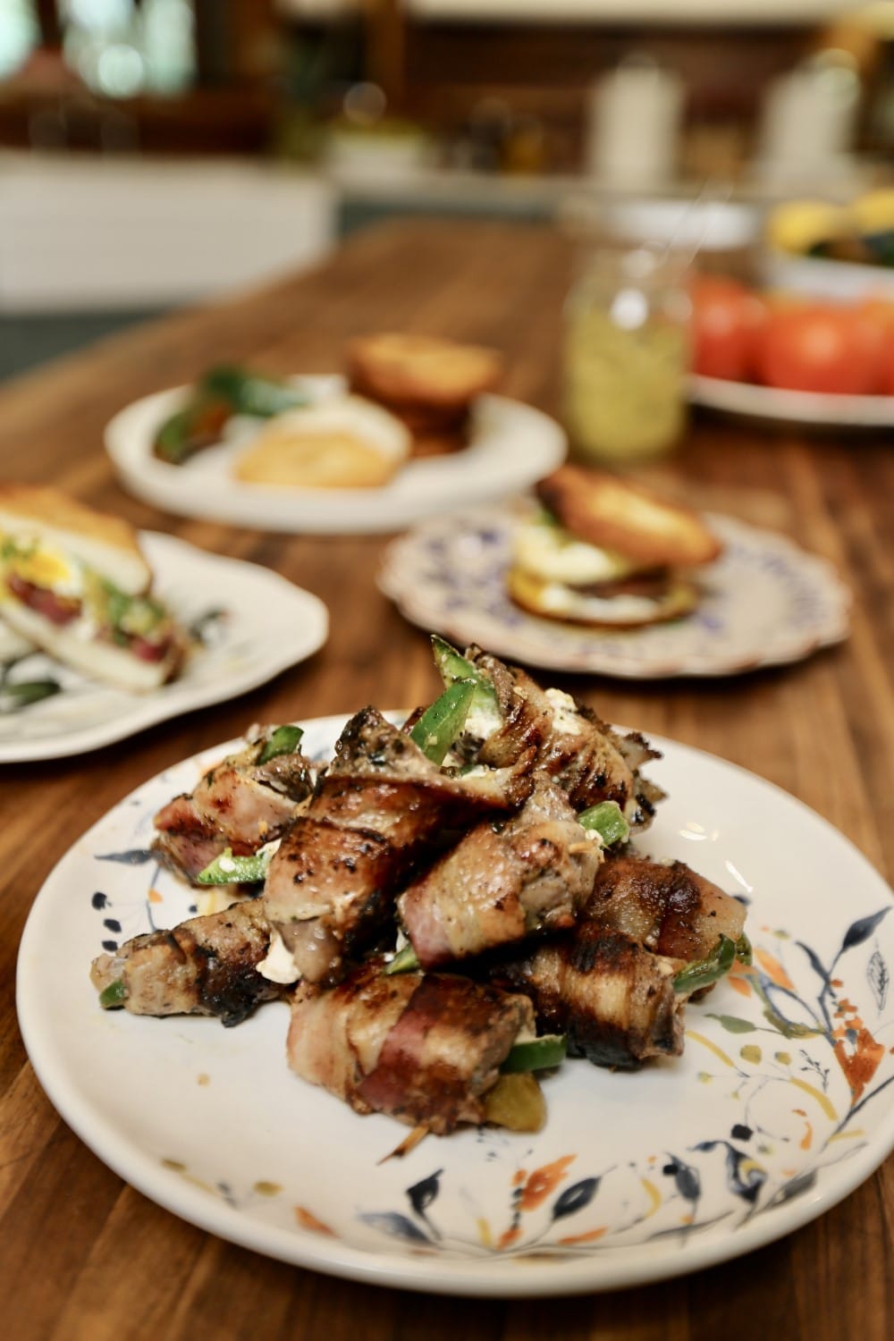Crispy bacon wrap around dove poppers on a white plate with delicate floral design, other plates blurred in background.