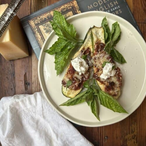 tomato and sausage stuffed zucchini on white plate sitting atop hardcover book