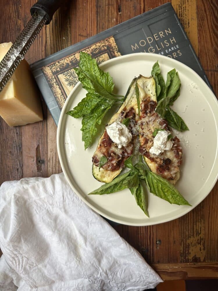 tomato and sausage stuffed zucchini on white plate sitting atop hardcover book