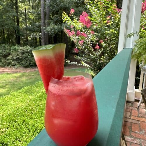 red watermelon lemonade drink with watermelon slice in clear glass on green railing of Stacy Lyn's porch