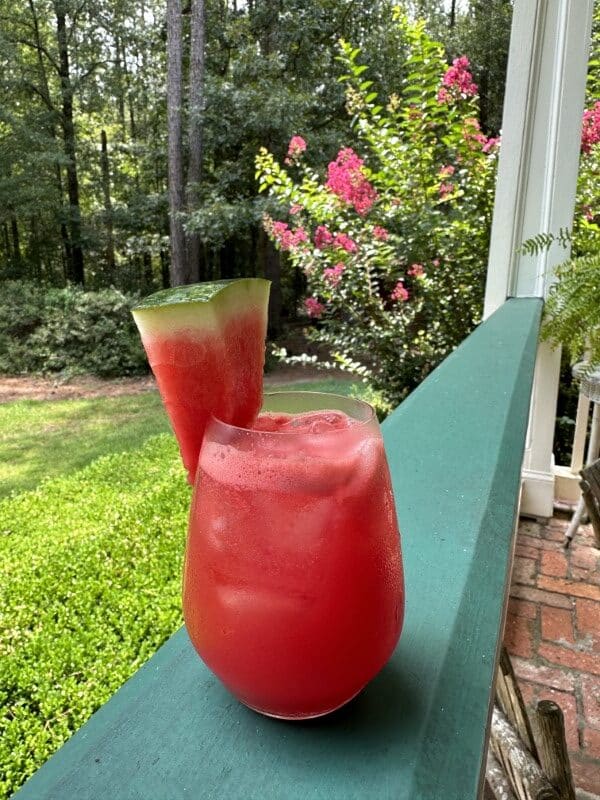 red watermelon lemonade drink with watermelon slice in clear glass on green railing of Stacy Lyn's porch