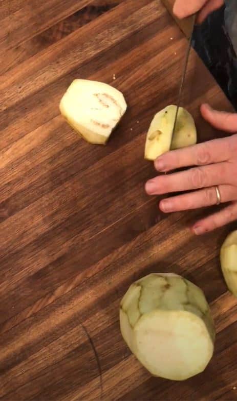 Stacy Lyn slicing peeled eggplant into cubed chunks on wooden cutting board