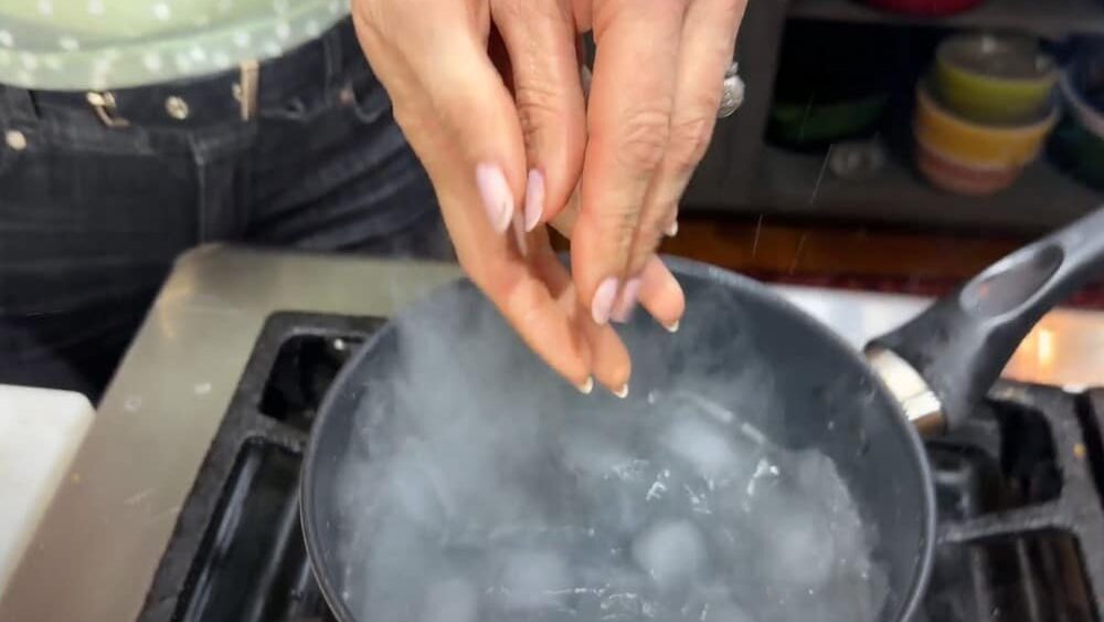 Stacy Lyn adding ice cubes to hot simple syrup in saucepan on stove