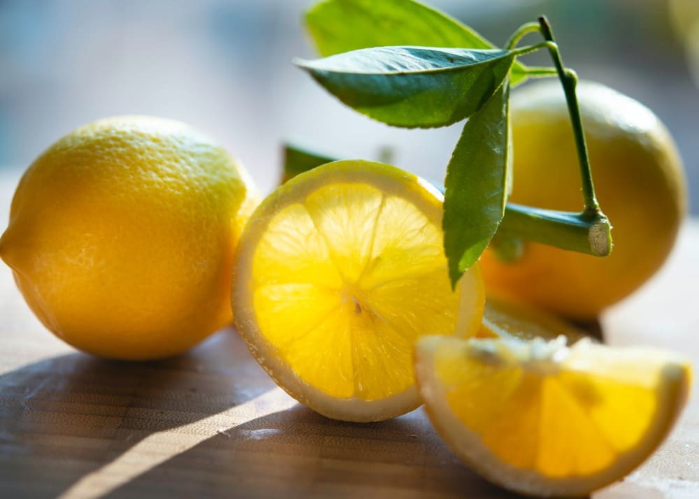 two whole and one sliced freshly picked lemon with green leaf stem